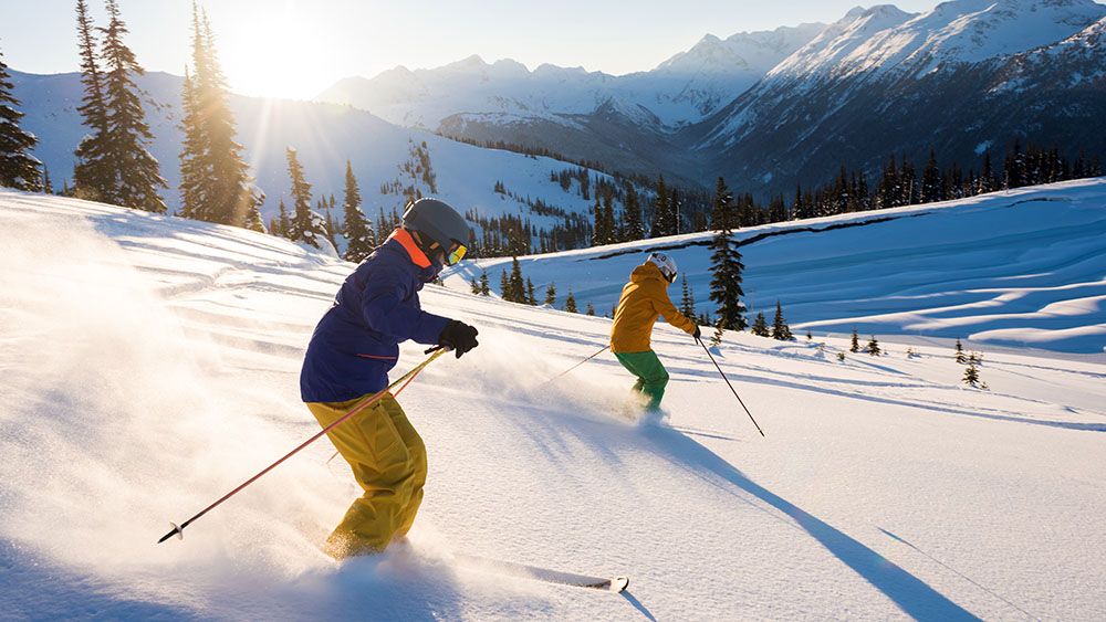Man and woman downhill snow skiing in mountains.